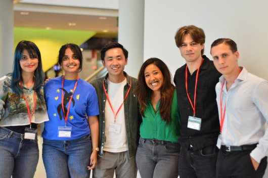 Six people posing together with red badges in The Hague.