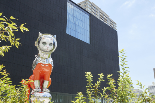 Shiny silver cat in a space helmet next to a modern building