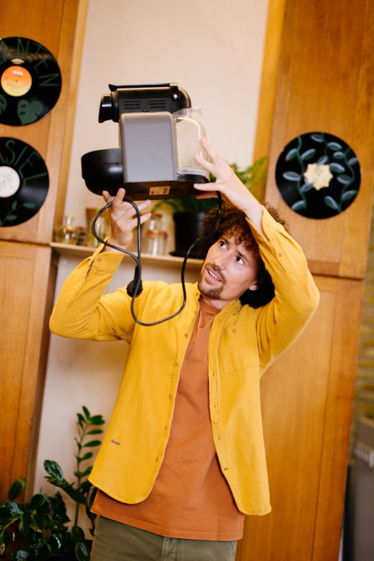 A man holds a kitchen appliance above his head.