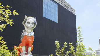 Shiny silver cat in a space helmet next to a modern building