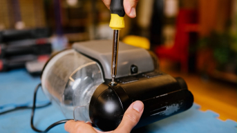 A hand using a screwdriver to repair a device.