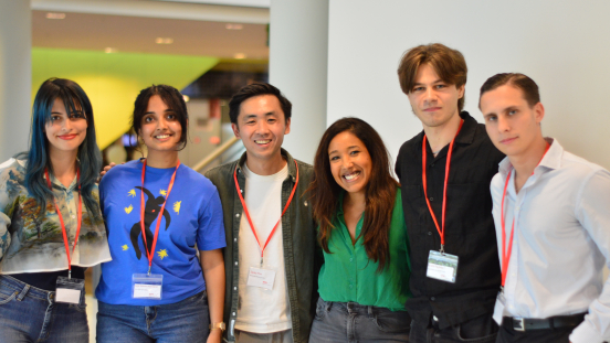 Six people posing together with red badges in The Hague.