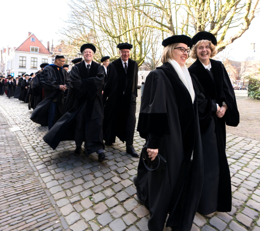 Group of academics in traditional attire walking down a street.