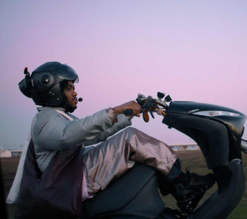 Een persoon rijdt met één wiel omhoog op een scooter bij zonsondergang.