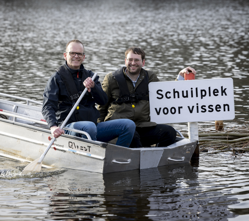 Two men sit in a boat next to a sign reading 'Shelter for fish'. Credit: Henriette Guest 