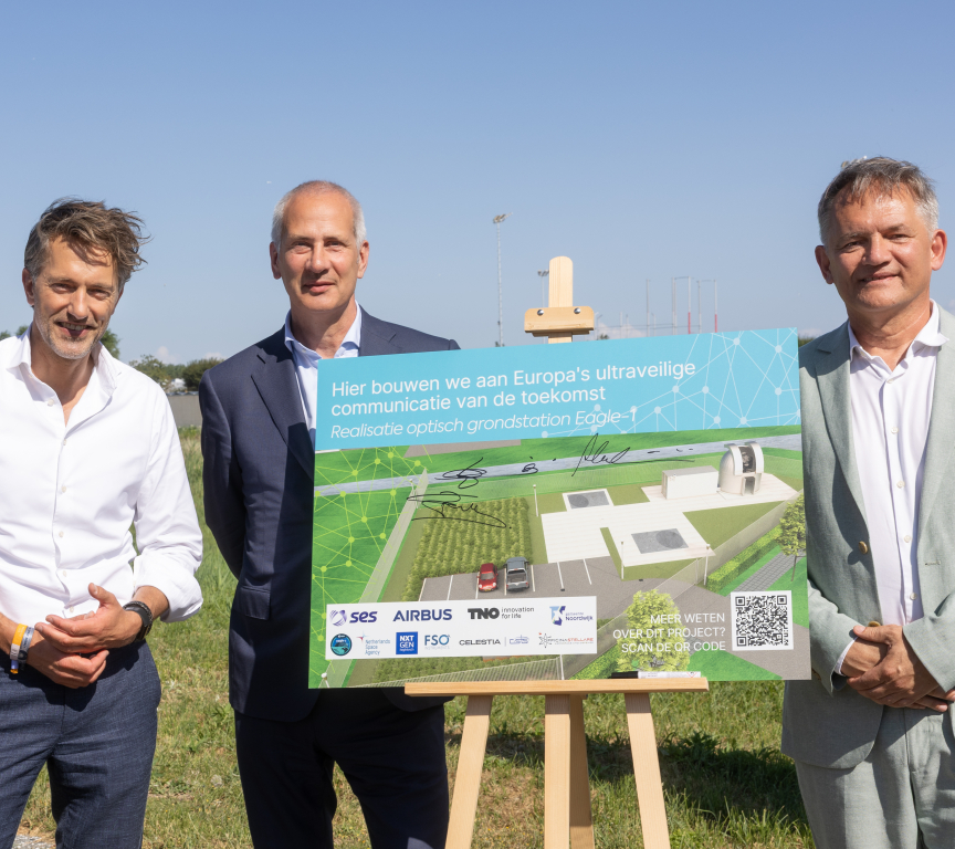 Three men stand next to an illustration of the future optical ground station