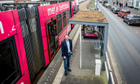 A man is standing at a bus stop on a street in The Hague.