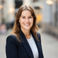 Woman with long brown hair, smiling in business outfit.