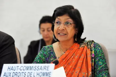 A woman in an orange and green sari speaks at a meeting.
