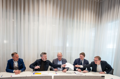 Vijf mannen ondertekenen gezamenlijk documenten aan tafel