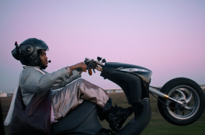 Een persoon rijdt met één wiel omhoog op een scooter bij zonsondergang.