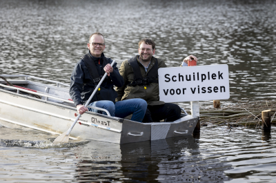 Two men sit in a boat next to a sign reading 'Shelter for fish'. Credit: Henriette Guest 