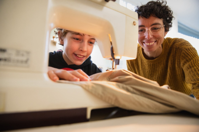 A child and an adult working together at a sewing machine.