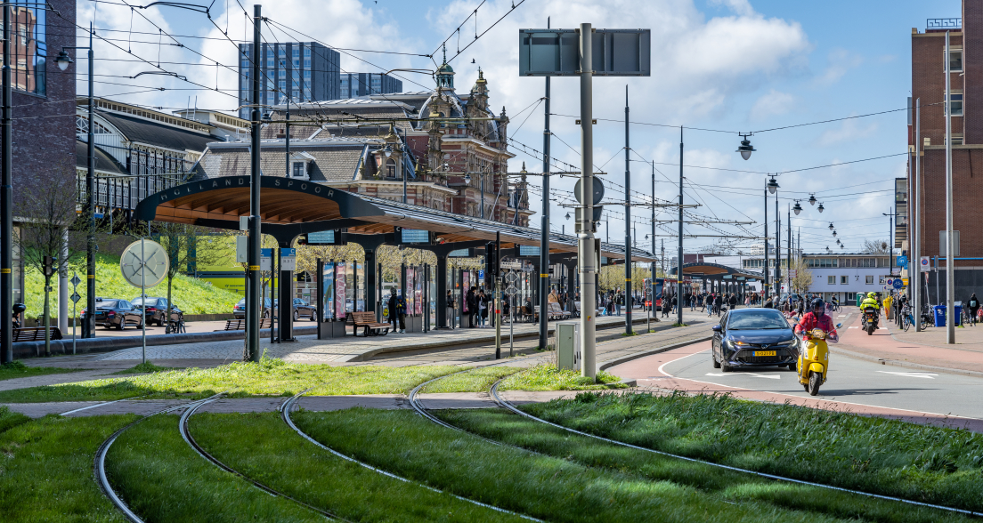 Busy tram stop at the station in The Hague, with passengers and vehicles. (c) Hugo de Wolf