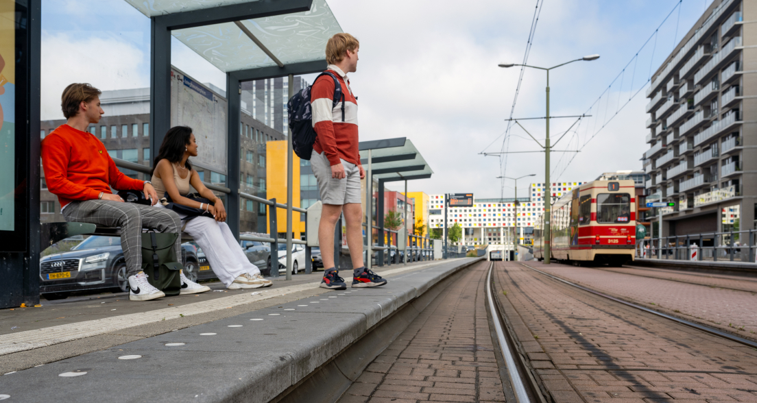 Three people waiting at a tram stop in an urban setting.