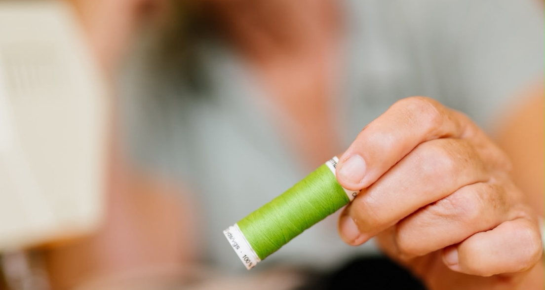 A woman holds a green thread spool next to pins.