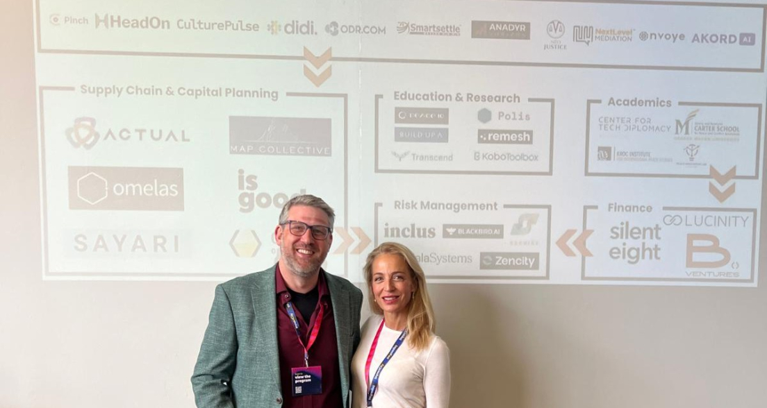Two people stand in front of a presentation about PeaceTech.