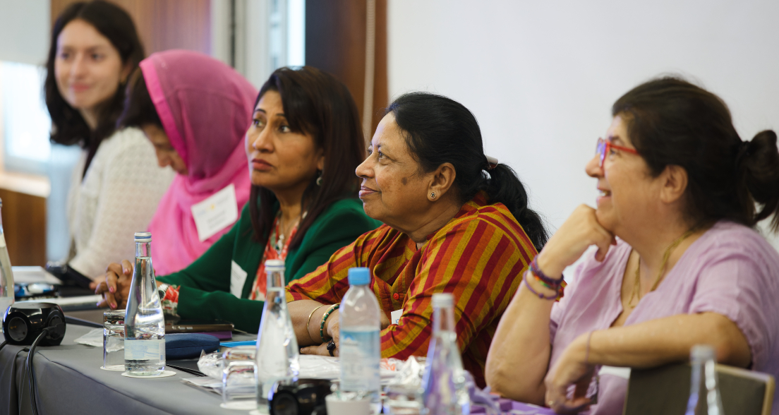 Women are sitting at a table in a meeting, with water bottles and notes.