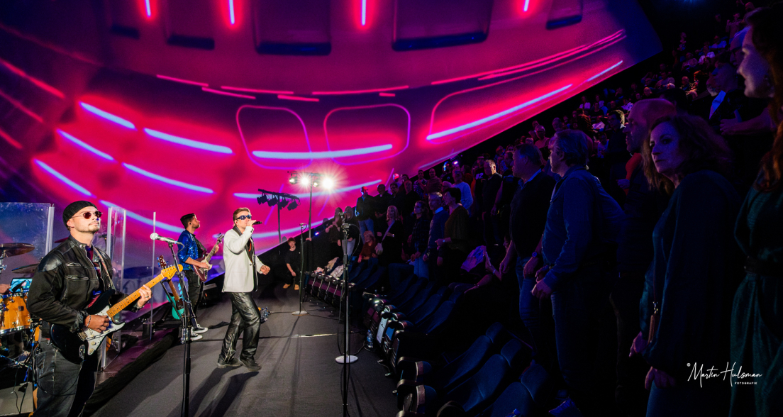 A band performs on stage with colorful lights and an enthusiastic audience.