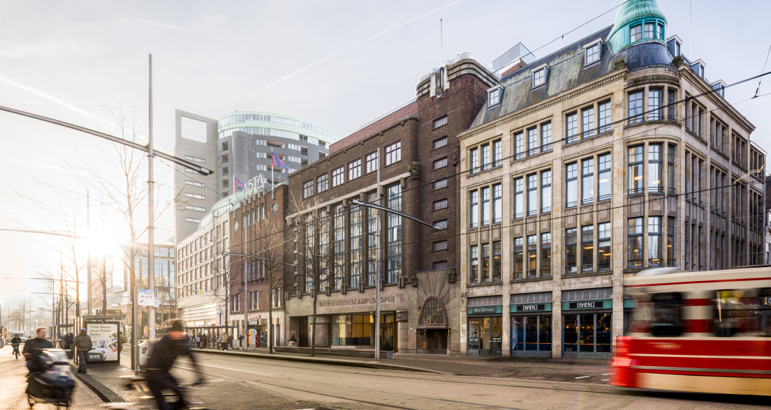 Facade of University Campus Spui with cyclists and tram in the foreground.