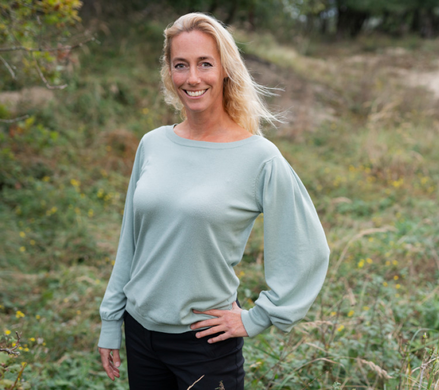 Woman with blonde hair in a green sweater, standing in the grass