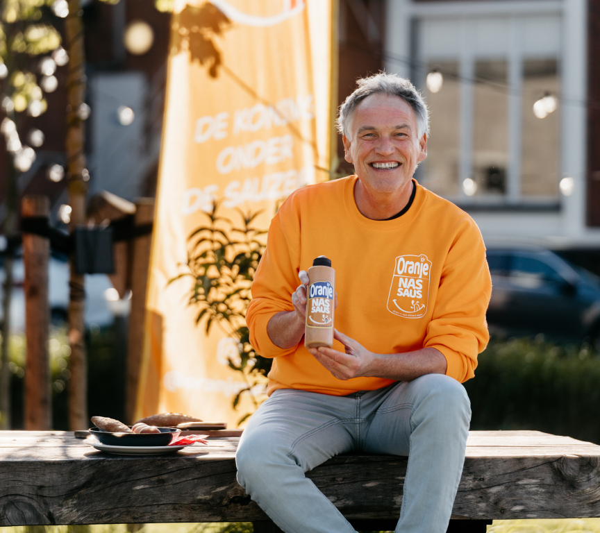Een man in een oranje trui toont een fles nas-saus.