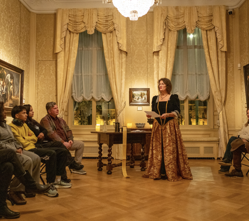 A woman in historical clothing presents to an audience in a hall.
