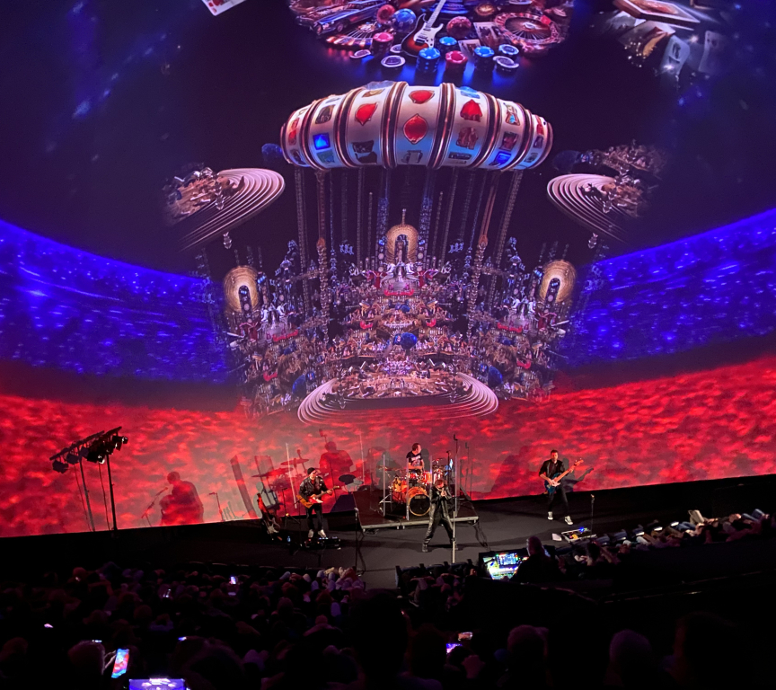A live band performs on stage with colorful projections in the background.
