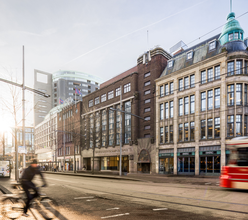 Facade of University Campus Spui with cyclists and tram in the foreground.