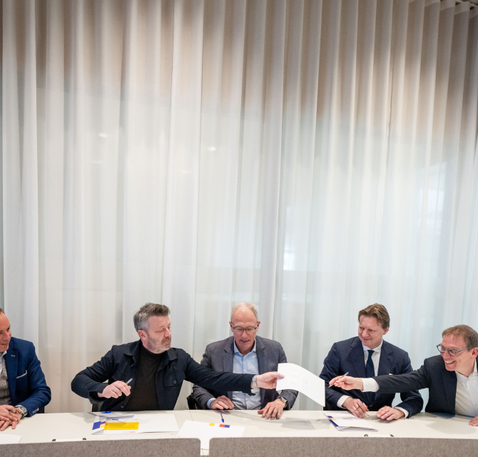 Five men jointly signing documents at a table