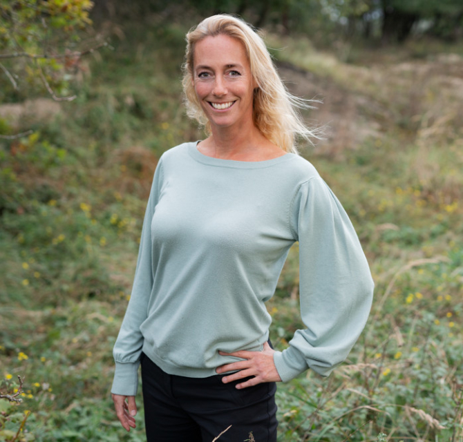 Vrouw met blond haar in een groene trui, staand in het gras
