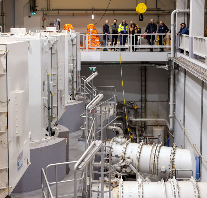 Technicians in a machinery room with large equipment.