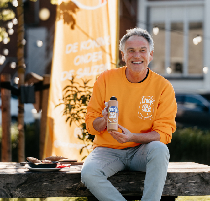 Een man in een oranje trui toont een fles nas-saus.