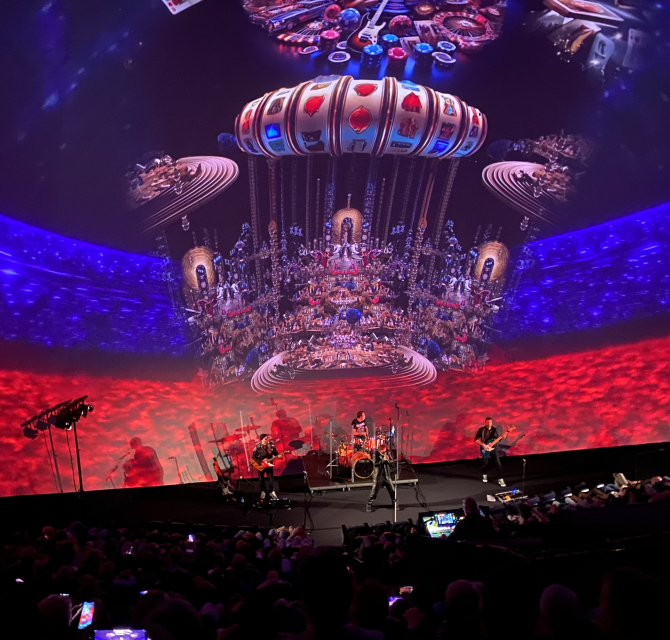 Een liveband speelt op een podium met kleurrijke projecties op de achtergrond.