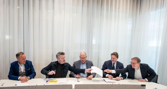 Five men jointly signing documents at a table