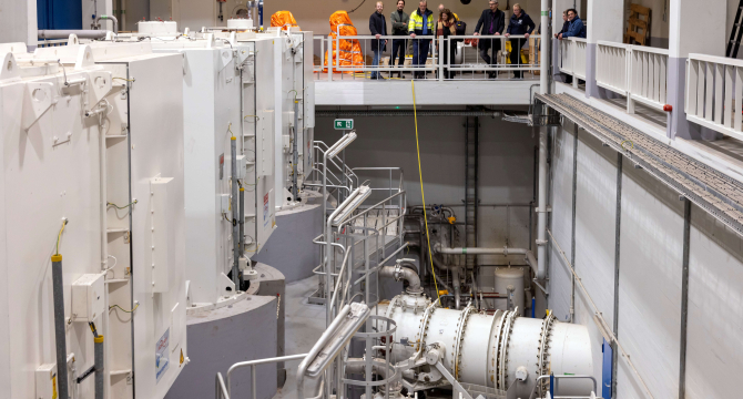 Technicians in a machinery room with large equipment.