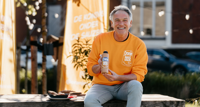 Een man in een oranje trui toont een fles nas-saus.