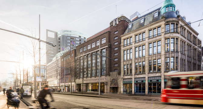 Facade of University Campus Spui with cyclists and tram in the foreground.