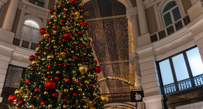 Grote kerstboom versierd met rode en gouden ornamenten.