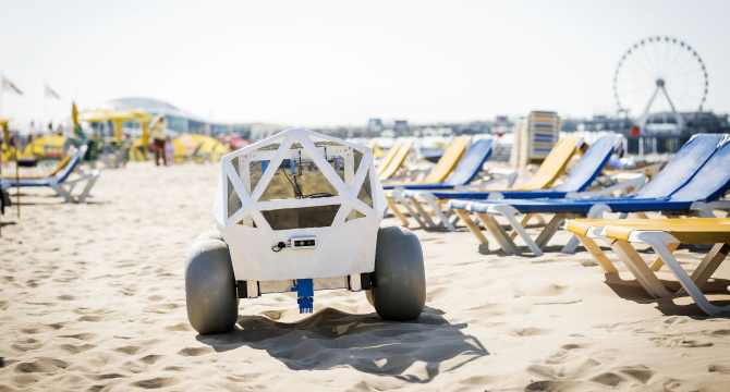 Een robot staat op het zandstrand met ligbedden op de achtergrond.
