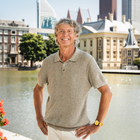A smiling man stands by the Hofvijver with buildings in the background.