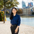 Een jongeman met donker haar en een blauwe blouse staat bij de Hofvijver in Den Haag.