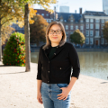 Een vrouw staat bij de Hofvijver met herfstbomen op de achtergrond.