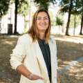Woman in a light-colored blazer standing outside in a park.