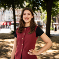 A smiling woman stands in a park with trees.
