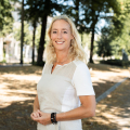 Woman with blonde hair standing and smiling in a park.