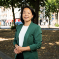 Woman with dark hair in a green blazer, standing in a park-like setting in The Hague.