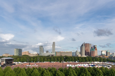 Een groot publiek bij een buitenconcert in Den Haag, met hoge gebouwen op de achtergrond.