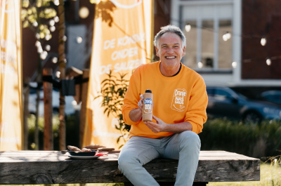 Een man in een oranje trui toont een fles nas-saus.