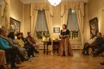 A woman in historical clothing presents to an audience in a hall.